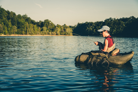 Fisherman fighting with big trout while floating with bellyboat on lake in Jesenice, Slovenia. Sunny summer day. Still water fly fishing and outdoor lifestyle theme.の写真素材