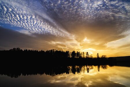 Sunset with orange and blue dramatic clouds and its reflection in water surface of lake in Vrbov,...