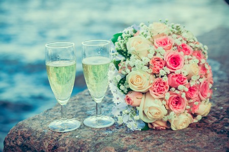 glass of champagne and a bouquet of the bride on a background of waterの写真素材