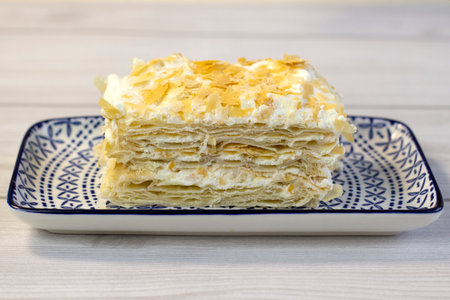 A piece of puff cake with cream on a rectangular plate with a pattern, close-up