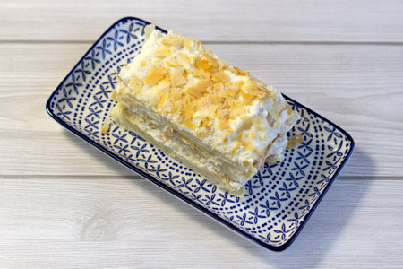 A piece of puff cake with cream on a rectangular plate with a pattern, close-up