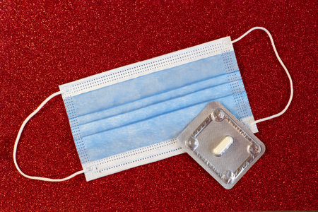Blister with one pill and mask close up on a bright red background, medicine