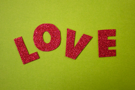 The inscription Love cut out of red glitter paper on a green texture background, close upの写真素材