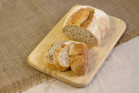 Appetizing freshly baked bread with a golden brown crust on wood cutting board a rough linen cloth...