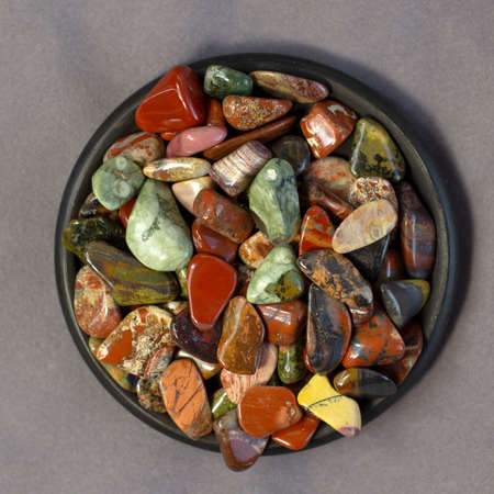 Red and multicolored jasper polished tumblestones on black plate and gray cloth top view
