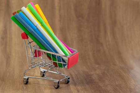 Small shopping cart with colored pencils on dark wooden background close upの写真素材
