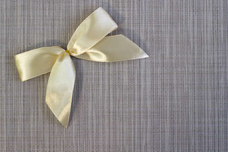 Bright gold satin bow on gray linen background with blank space