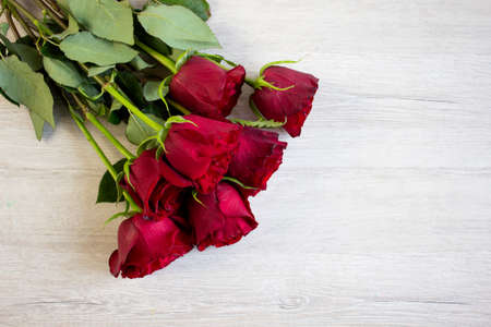 Beautiful bouquet of dark red roses on light wooden background, closeup with copyspace top viewの写真素材