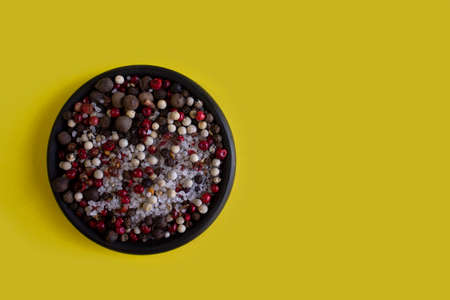 Spices, white, black and red peppers, sea salt on black plate on a yellow background, close-up top viewの写真素材