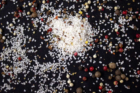 Spices, white, black and red peppers, sea salt sprinkled on a black background, close-up