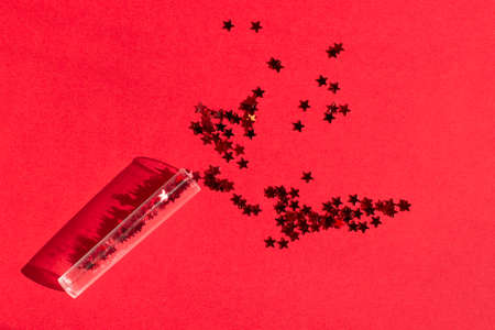 Sequins tube scattered red stars glitter on red textured background close up