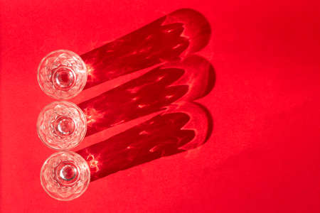 Beautiful crystal glasses with shadows on a bright red background, close-up
