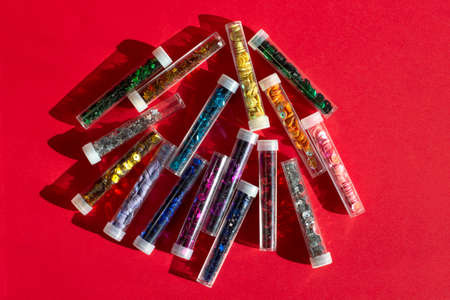 Sequins tube scattered red stars glitter on red textured background close up