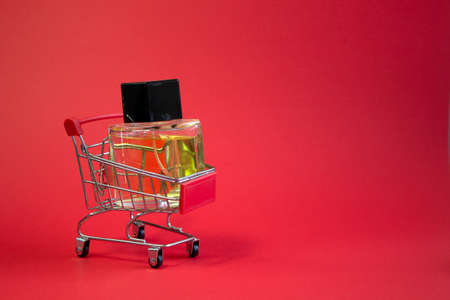Shopping cart with perfume on red background minimalism, the concept of beauty, accessories with empty spaceの写真素材