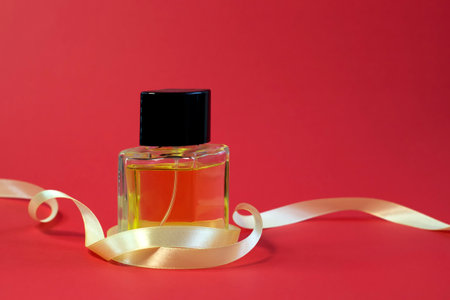 Beautiful bottle of perfume on bright red background with ribbon close-up front viewの写真素材
