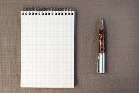White spring notepad and marble pen with blank space for writing on brown gray textured background...