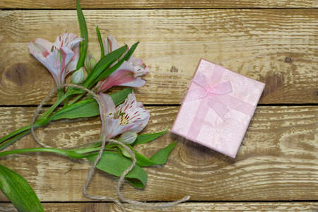 Bright white and pink flowers Alstroemeria and pink paper wrapped gift box on wooden textured background close-upの写真素材