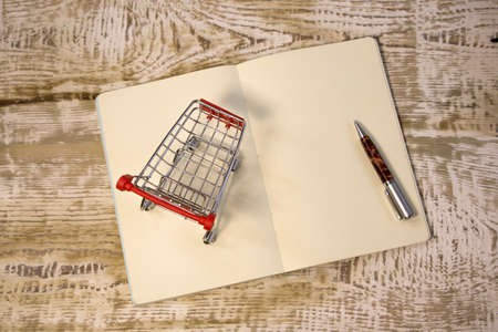 White blank notepad and small shopping cart trolley on bright red background close up front view...