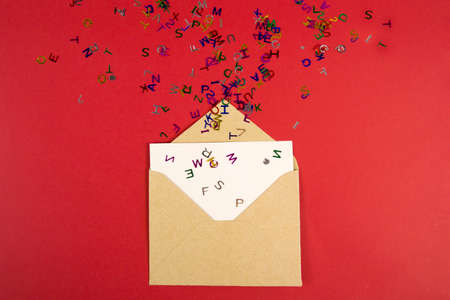 Bright multicolored small letters scattered on bright red background with envelope flat lay