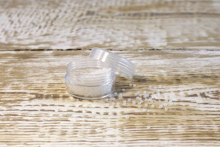 White beads for needlework. Pearl color in plastic jar. On white pine wooden boards front view