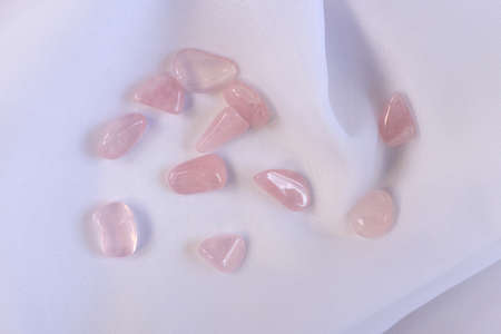 Several pieces of polished pink quartz on white textured fabric background. Minimal color still life...