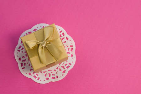 Closed golden gift box with silk gold ribbon bow on bright pink background close upの写真素材