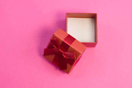 Open red gift box with silk gold ribbon bow on bright pink background close upの写真素材