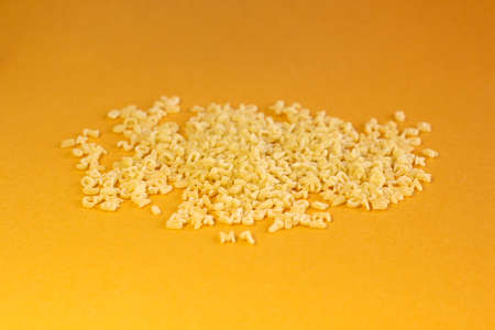 Whole grain dark pasta letters on dark yellow textured background with selected focusの写真素材