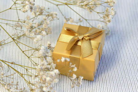Closed golden gift box with silk gold ribbon bow onon white knitted background close upの写真素材