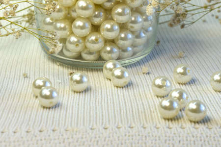 Bright beautiful whitw pearl beads scattered on white knitted textured background, close up