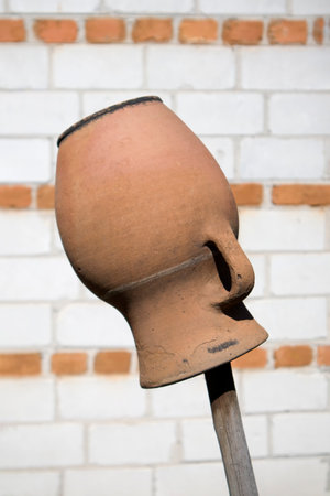 Old clay pot isolated on wooden stick on blurred brick background
