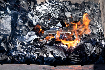 A wooden cross is burning with fire against black ash top view