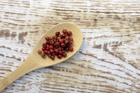 Red or pink peppercorns on wooden spoon on gray textured cutting board background top view