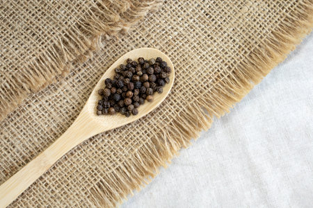 Pile of Black peppercorns Black pepper dried seeds in wooden spoon on linen background close up top viewの写真素材