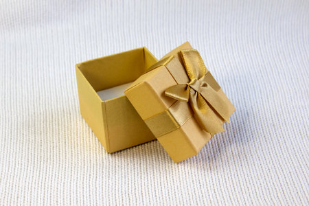 Opened gold gift box with silk golden ribbon bow on white knitted background