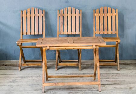 Wooden table and three chairs on the wooden floor. In the background is a light blue wallの写真素材