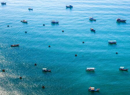 Small and large boats of Vietnamese sailors in the blue sea. The left corner is the reflection of the sun on the waterの写真素材