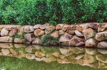 On the shore, green leaves of trees and granite stones with an orange tint to strengthen. All this is reflected in the surface of the riverの写真素材