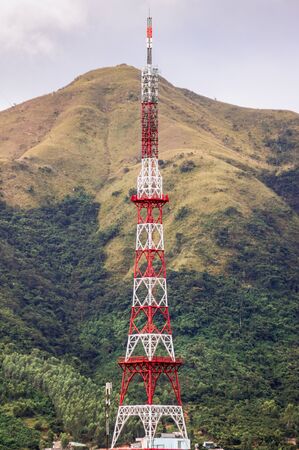 The metal tower of the base station of cellular communications and public networks with a mast for radio communications. In the background a high mountainの写真素材