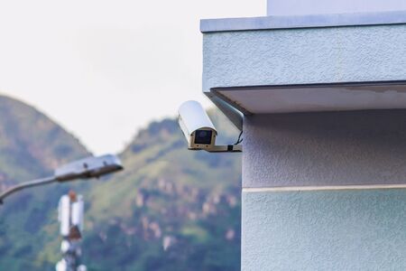 A security camera in a protective metal case is installed on the corner of the house with blue...