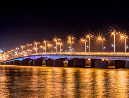 Nha Trang city. Automobile bridge over the river with lanterns shining with orange light. In the foreground is water. Long Shutter Shootingの写真素材
