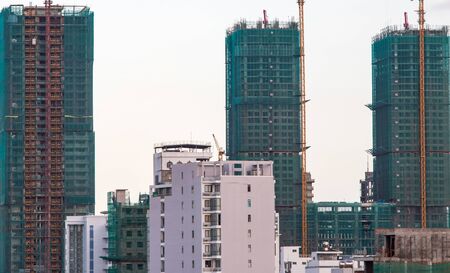 In the foreground is a multi-story building, and in the background is a building of three unfinished skyscrapers covered with a green grid. The main background is the skyの写真素材