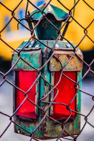 In the foreground is a rusty metal fence, followed by an old railway lamp with red glass.の写真素材