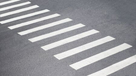 On the gray asphalt, the white lines of the pedestrian crossing are located diagonallyの写真素材