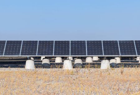 A row of blue solar panels on concrete poles. Blue sky background