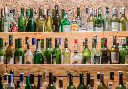 Cam Ranh, Khanh Hoa Province, Vietnam - July 14, 2019: Tops of empty glass bottles of various types of alcohol are visible on three wooden shelves. Top row in focusのeditorial素材