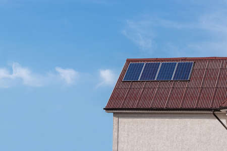 Four solar panels are installed on the roof slope of the house. The slate is red. Against the background of a blue sky with clouds.の写真素材