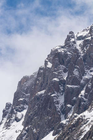 Picturesque rocky slopes covered with snow and fog. Against the background of a blue sky with cloudsの写真素材