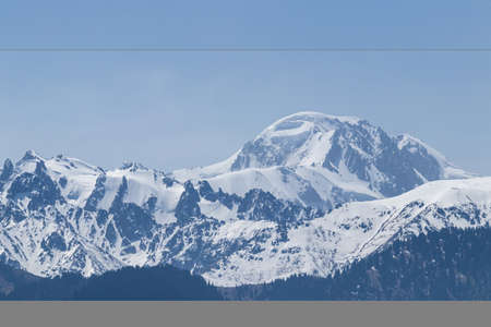Snowy mountain peak on a sunny day with avalanches on the slope. Against the blue skyの写真素材
