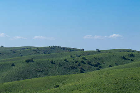 View of the green meadows of the mountain hills. Against the background of blue sky and cloudsの写真素材